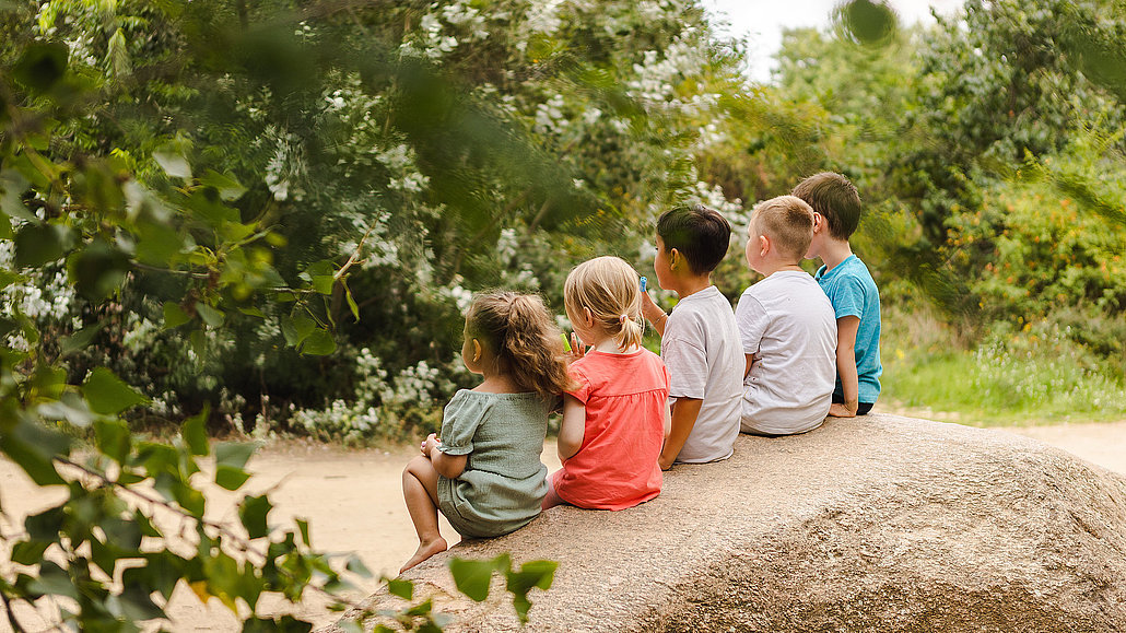 Fünf kleine Kinder sitzen auf einem großen Findling im Naturerfahrungsraum im Park am Gleisdreieck