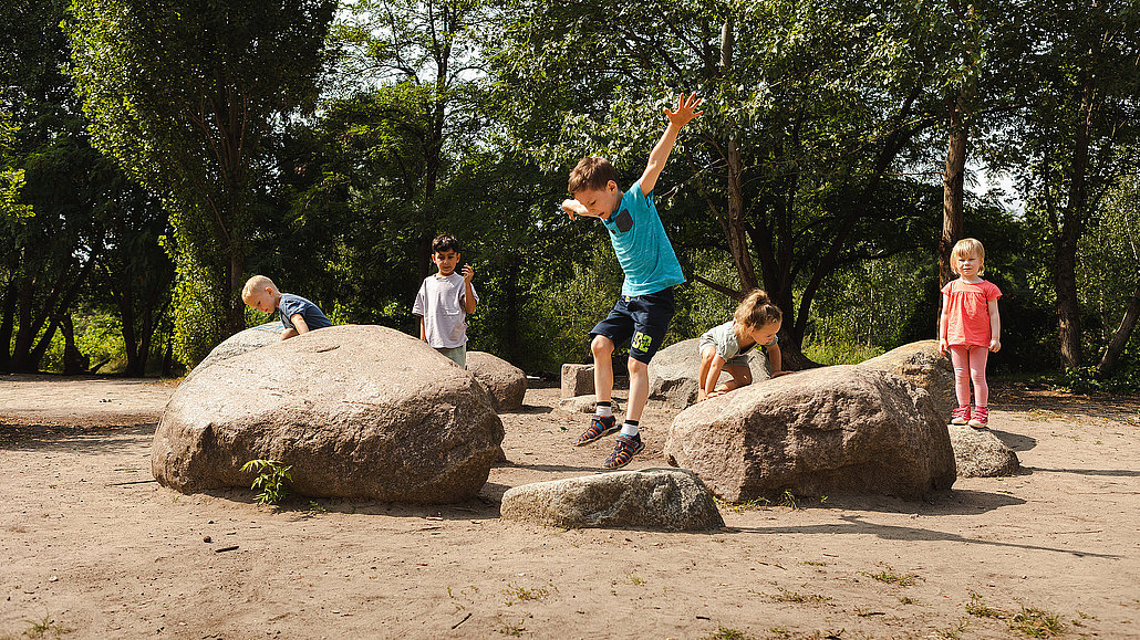 Kinder springen im Naturerfahrungsraum im Park am Gleisdreieck von einem Stein auf den anderen